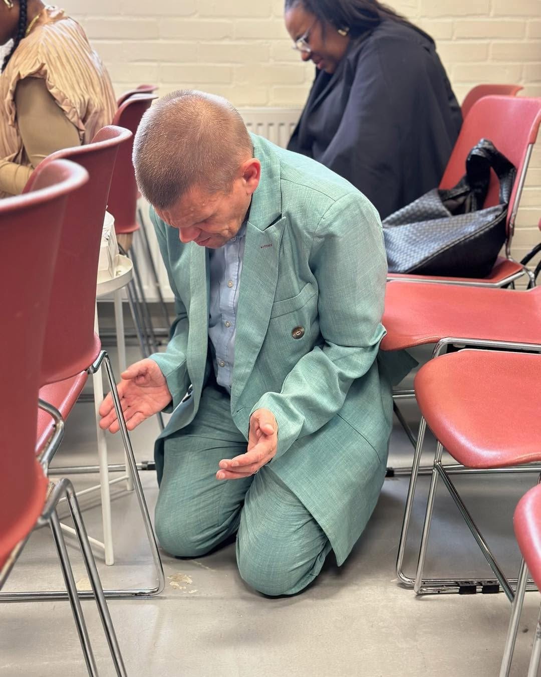 Een man knielt in gebed tussen de stoelen